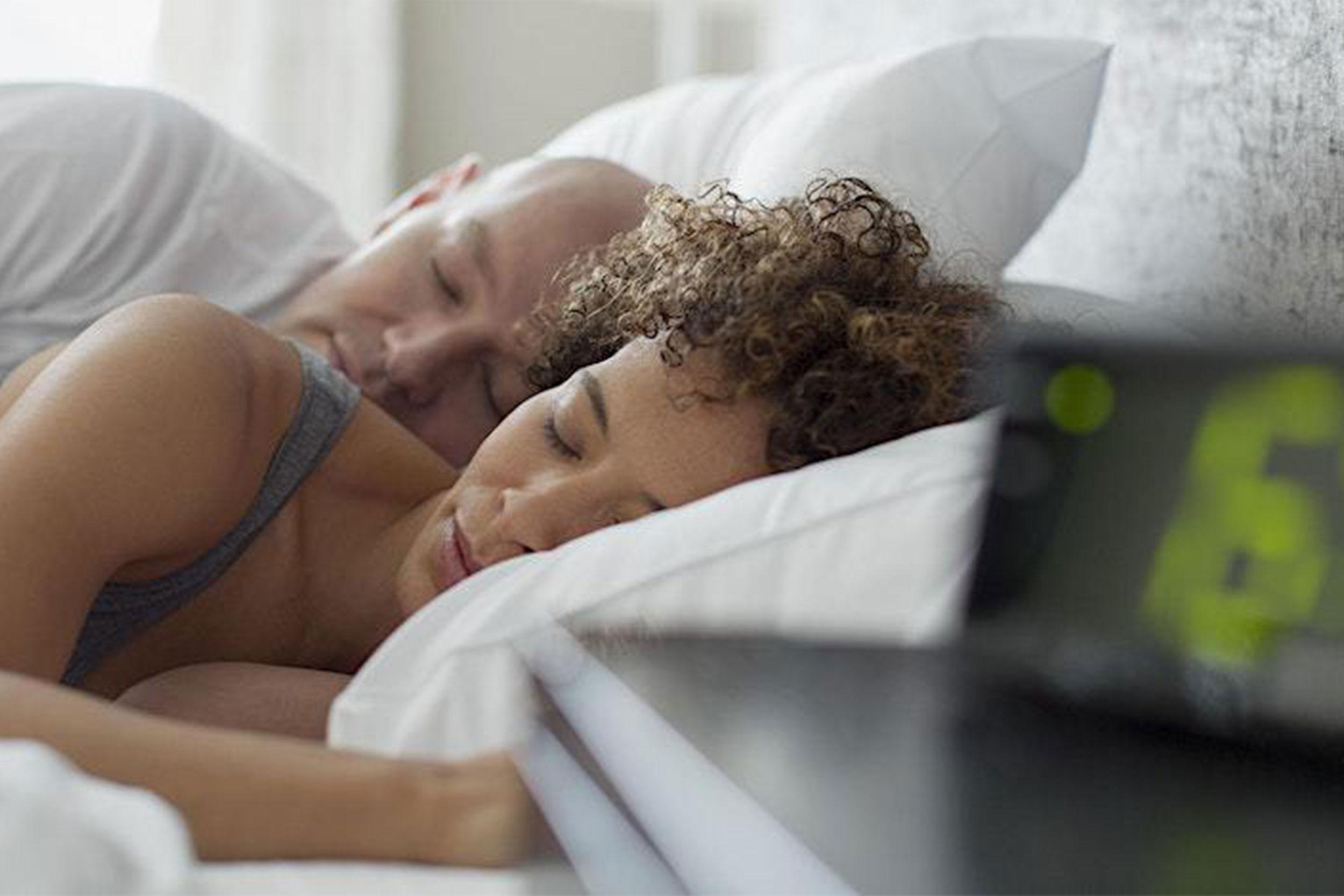 Man and woman sound asleep in bed next to digital alarm clock