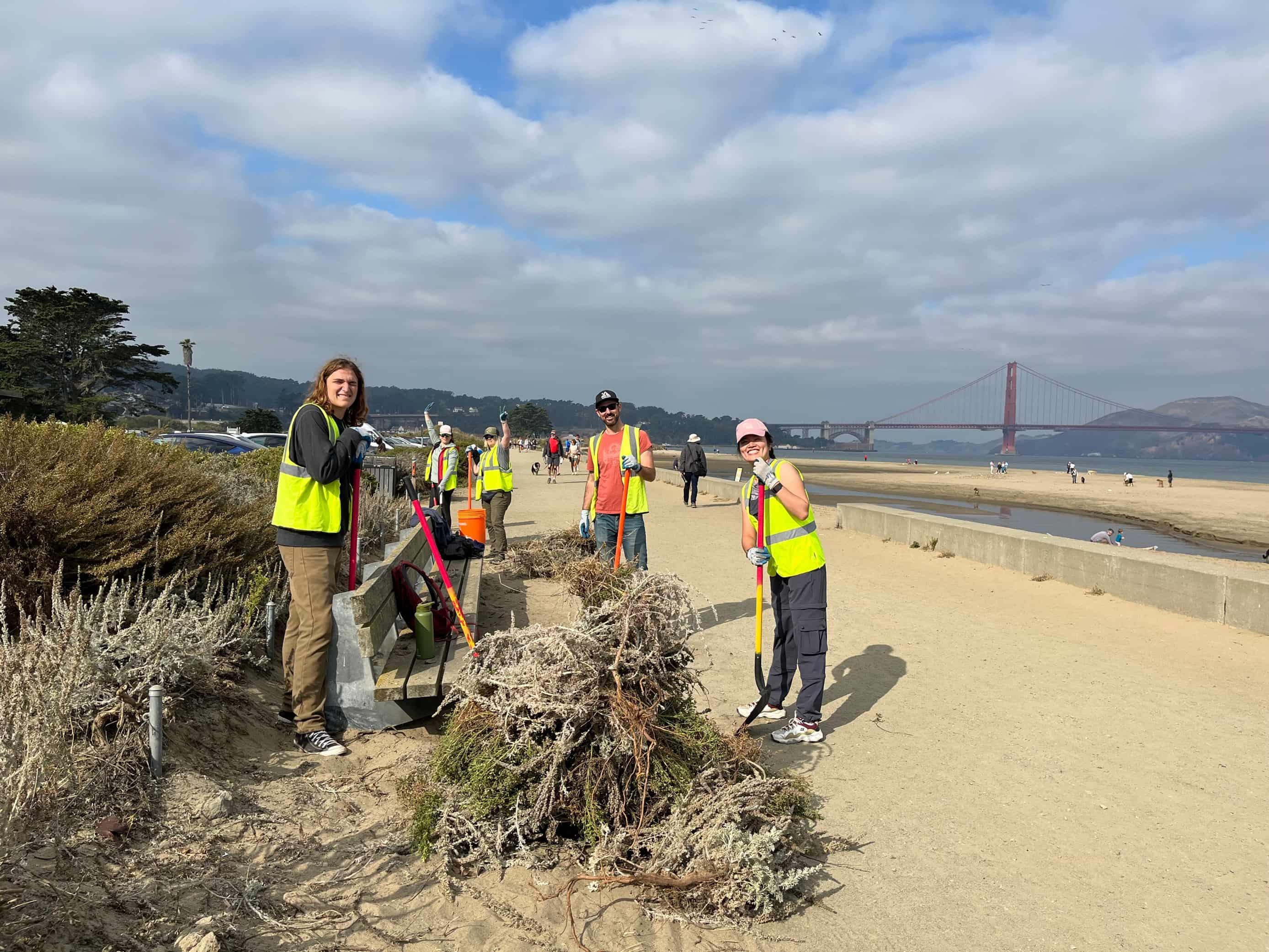 San Francisco Habitat Stewards at Crissy Field East Beach with shovels and the Golden Gate Bridge behind them.
