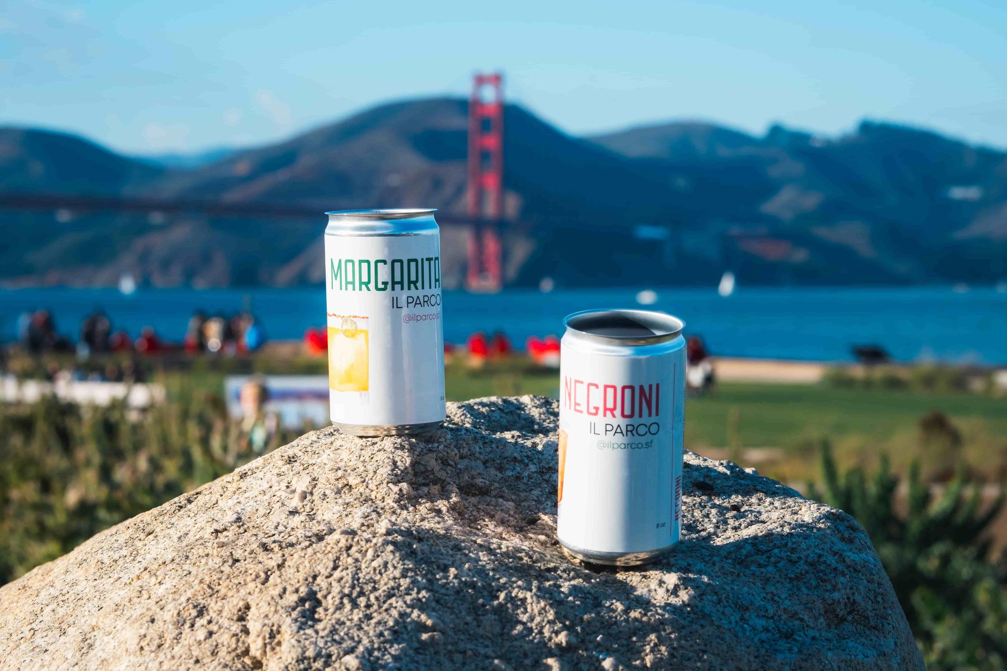 Two cocktails in a can made by Il Parco positioned on a rock at Presidio Tunnel Tops with the Golden Gate Bridge in the background.